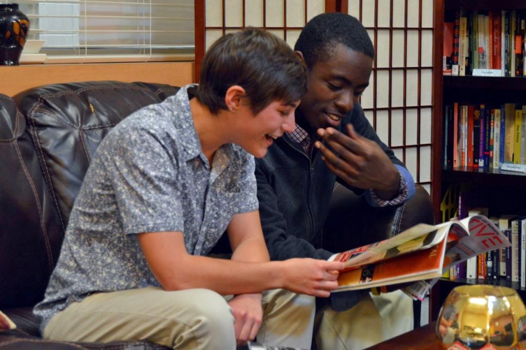 Two students sit next to each other on a leather couch and laugh at a magazine